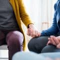Midsection of men and women sitting in a circle during group therapy.