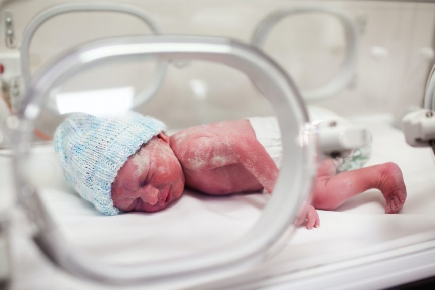 Newborn baby covered in vertix in incubator