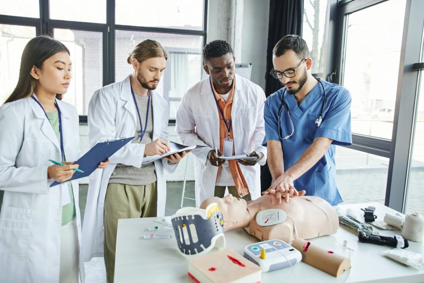 medical instructor showing chest compressions on CPR manikin near defibrillator, medical equipment