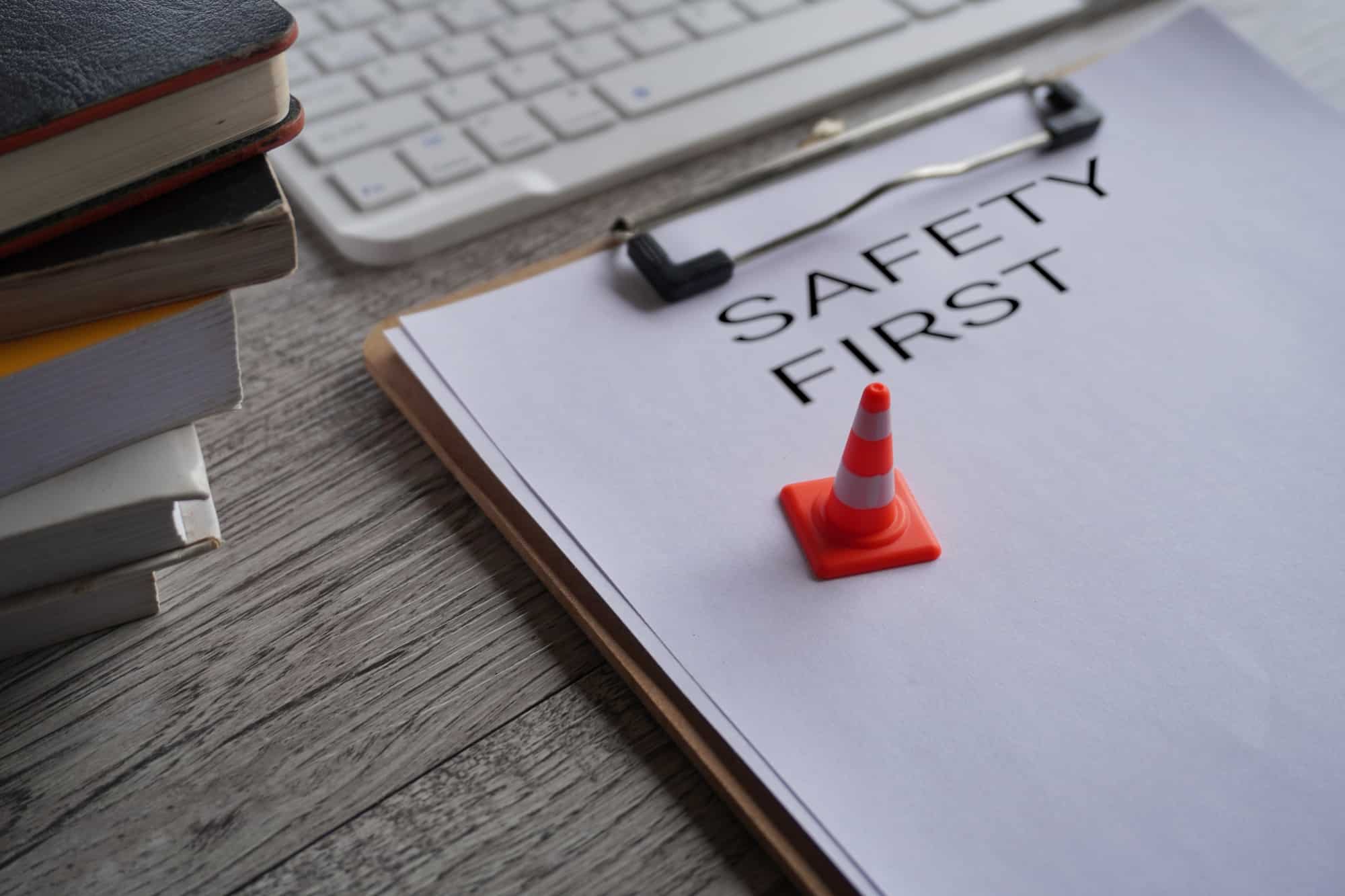 Miniature safety cone on top of paper clipboard with text SAFETY FIRST.